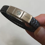Memorial ashes captured in a pawprint on a braided black leather bracelet