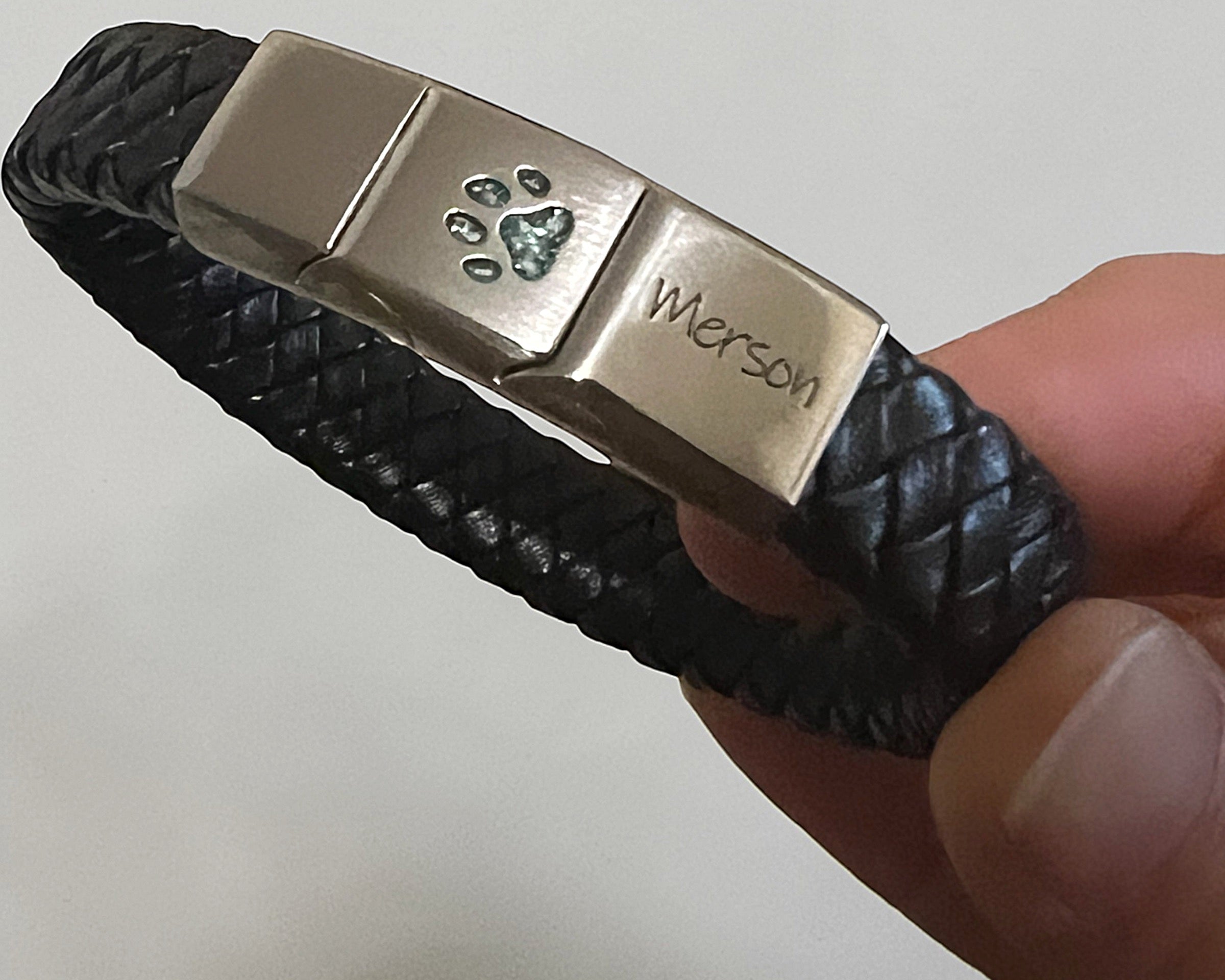 Memorial ashes captured in a pawprint on a braided black leather bracelet